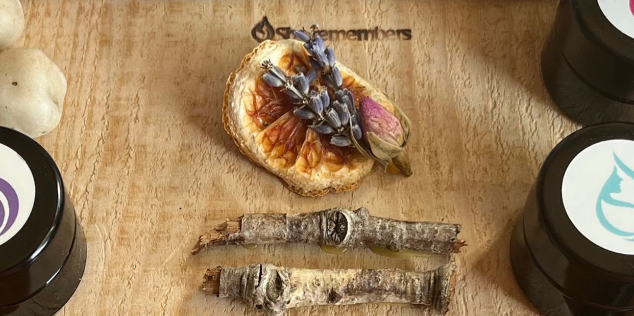 Close up of dried lavender, orange slice and rose bud on a piece of wood with words She Remembers