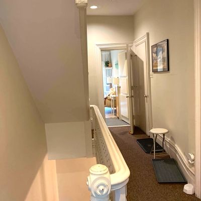 A cozy hallway with beige walls, carpet, and open doors leading to a well-lit room.