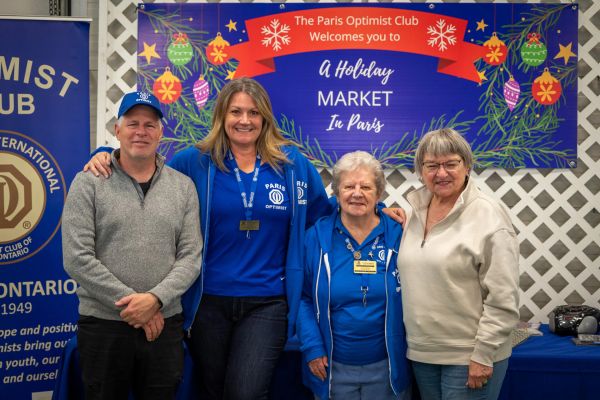 Four people smiling at a holiday market hosted by the Paris Optimist Club.