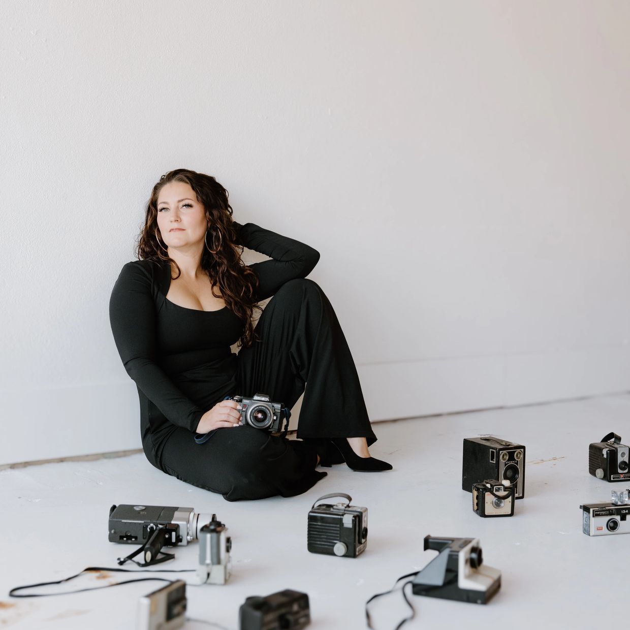 Woman in black outfit sitting with vintage cameras.