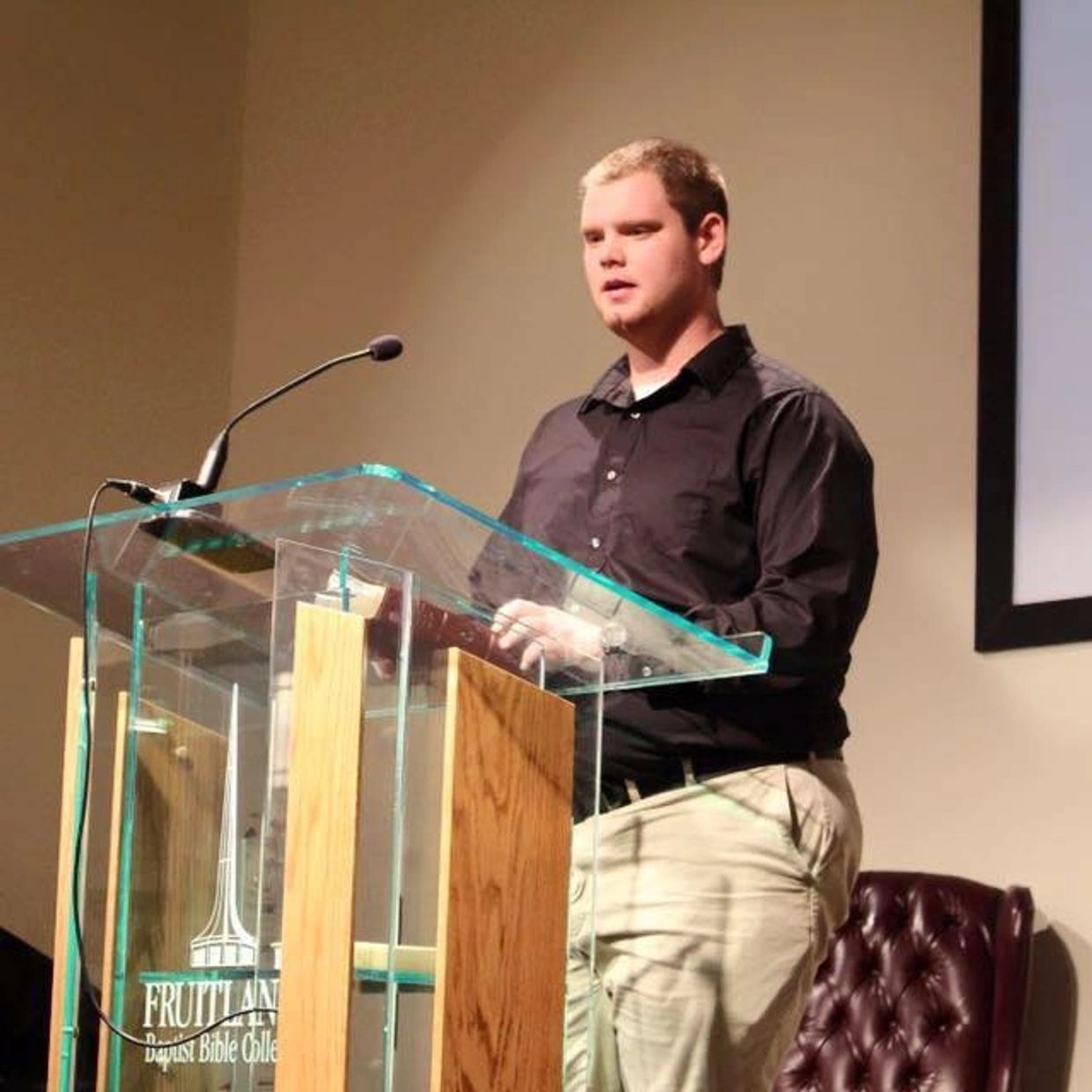 A man speaks at a clear podium in a church setting.