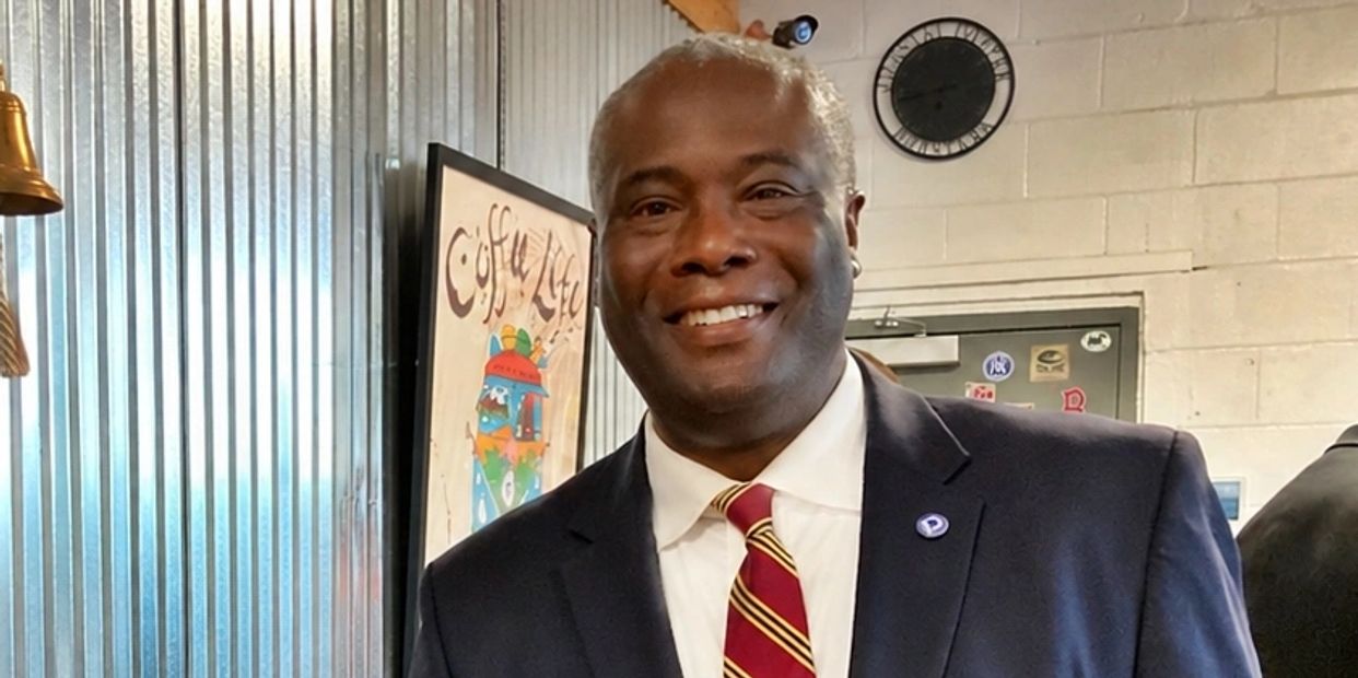 Man in suit smiling indoors with clock on wall.