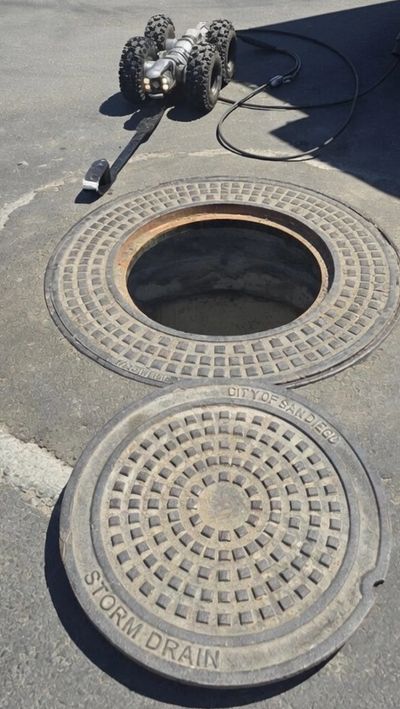 Open storm drain cover with an inspection camera nearby.