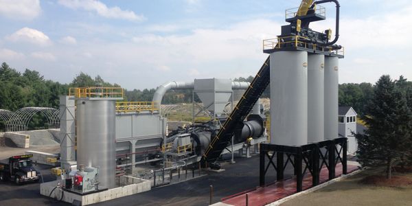 Industrial asphalt plant with silos and conveyor belt.