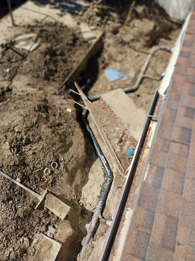 Excavation site with exposed piping near a tiled path.