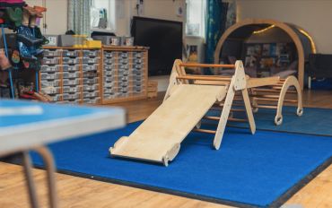 Indoor play area with wooden climbing frame and slide.