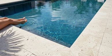 Relaxing poolside scene with feet dipped in water and lounge chairs.