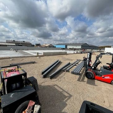Construction site with steel beams and equipment under cloudy sky.