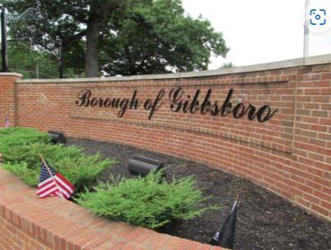 Brick sign reading 'Borough of Gibbsboro' with small flags and greenery.