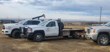 Three trucks parked on a gravel lot with a wide landscape in the background.