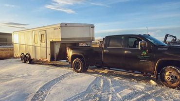 Black pickup truck towing a large white trailer on a snowy road.