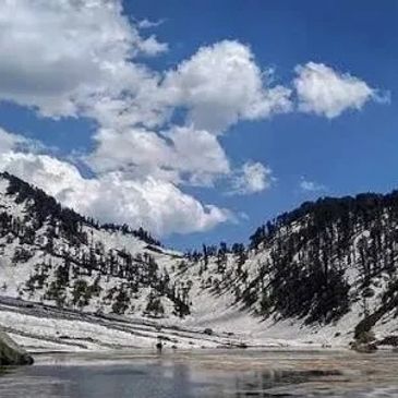 Snow-covered mountain valley under a blue sky with clouds.