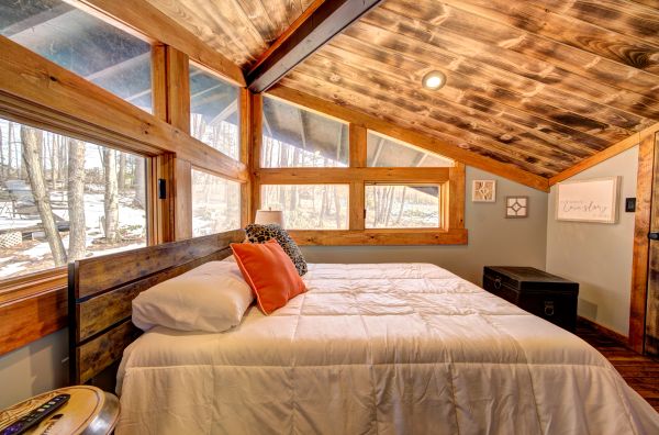 Cozy bedroom with large wooden windows and a sloped wooden ceiling.