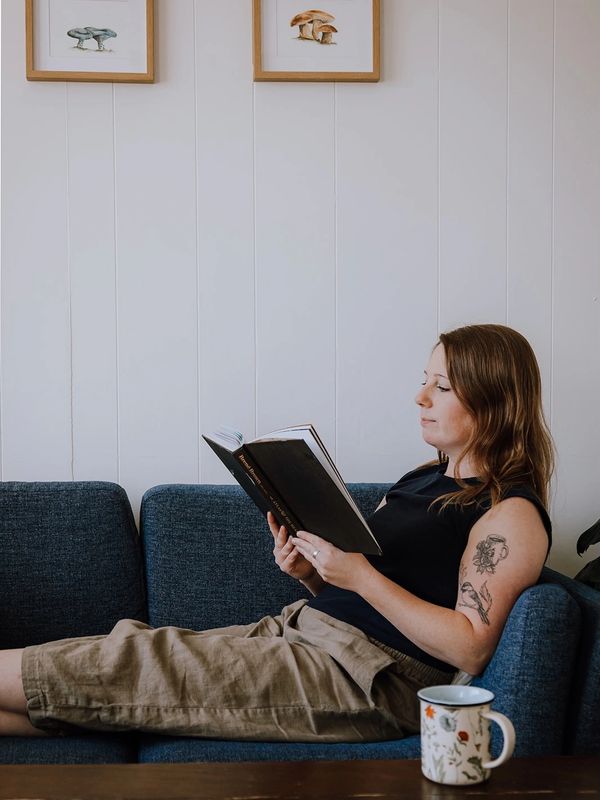 Woman with tattoos reading on a blue couch.