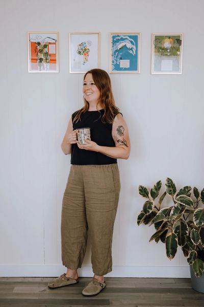 Woman standing with a mug, smiling.
