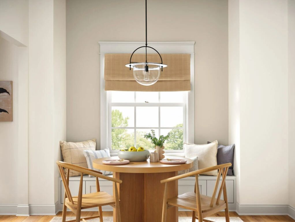 Cozy dining nook with wooden table, chairs, and cushioned window seat under a modern pendant light.