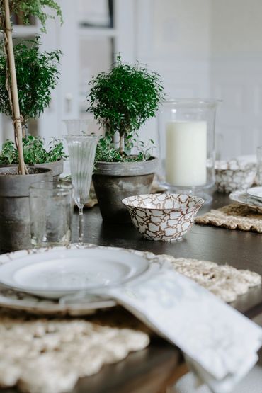Elegant table setting with potted plants, patterned bowls, and a white candle.
