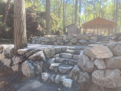Natural boulder retaining wall and stone steps built into slope at Fairytale Landscaping & Drainage.