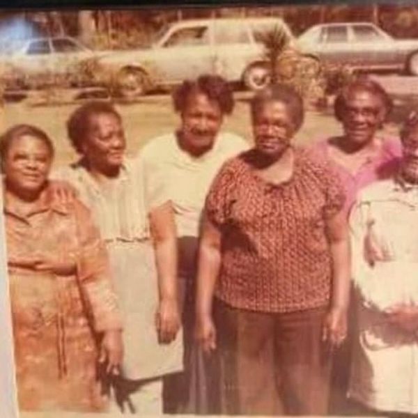 A group of six women posing outdoors on a sunny day.