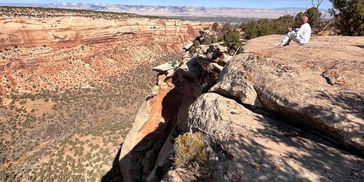 Dutch Harwell practicing energy clearing and reinforcing Emotional Navigation in white meditating on a rocky cliff overlooking a vast canyon under a blue sky.