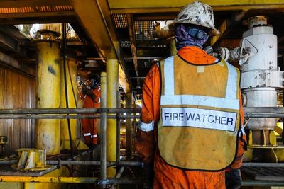 Worker in protective gear labeled 'Firewatcher' inside industrial facility.