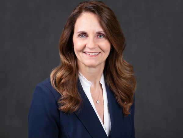 Professional woman in a navy blazer smiling against a dark background.