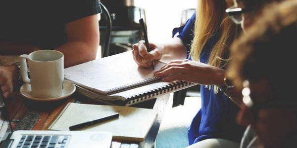 People collaborating and taking notes around a table with coffee and laptop.