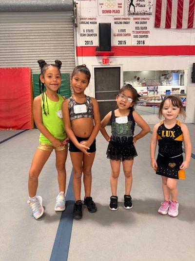Four young girls in cheerleading outfits posing indoors at a gym.