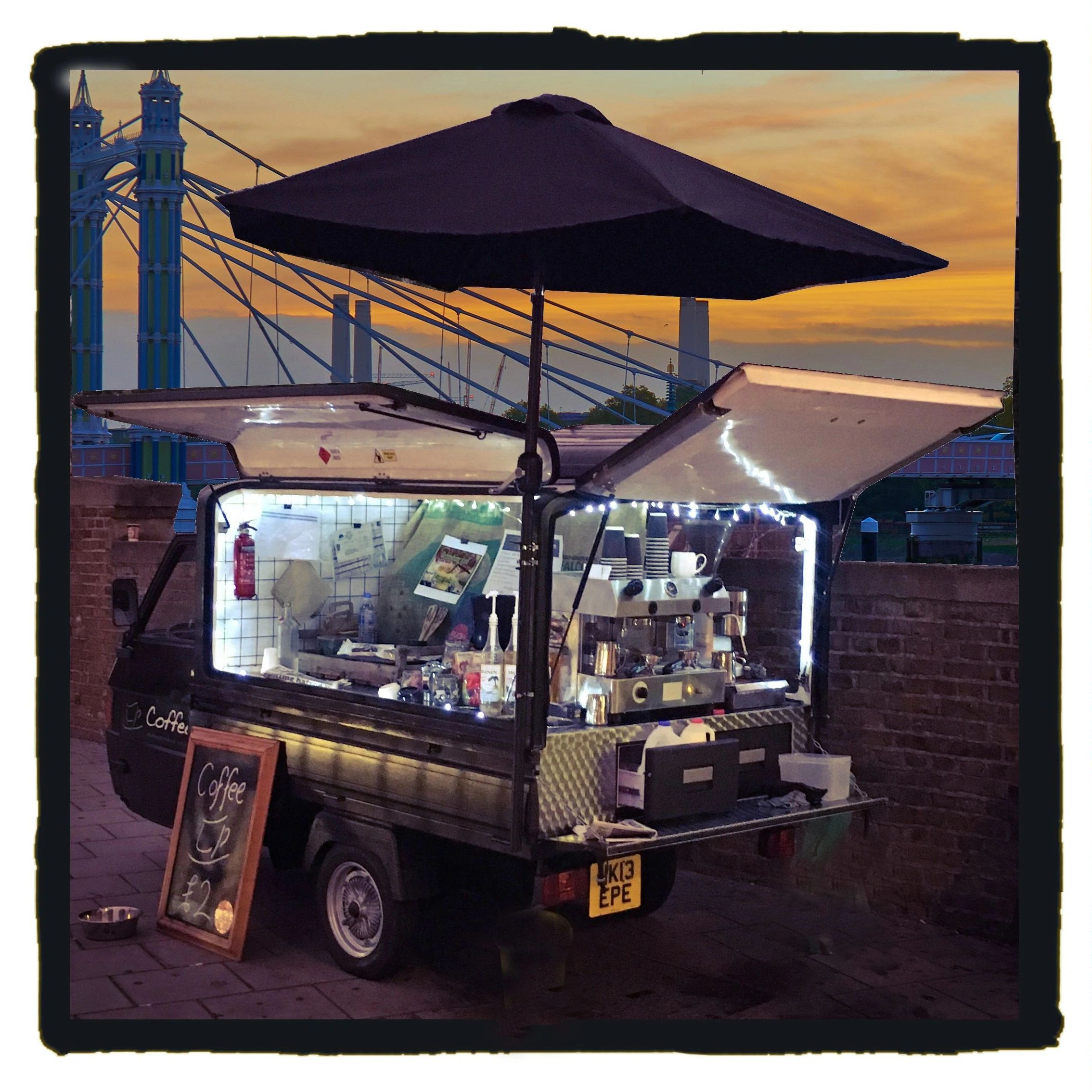 Mobile coffee cart illuminated at sunset with umbrella and chalkboard sign.