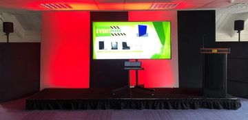 TV screen and smart lectern on stage with speakers and coloured lighting