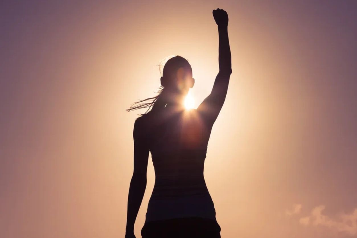An inspirational picture of the outline of a woman raising her left arm basking in the glowing  sun