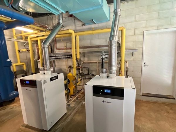 Two white industrial heating units with ventilation pipes in a utility room.