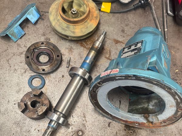 Disassembled mechanical pump parts on a workbench with boots visible below.