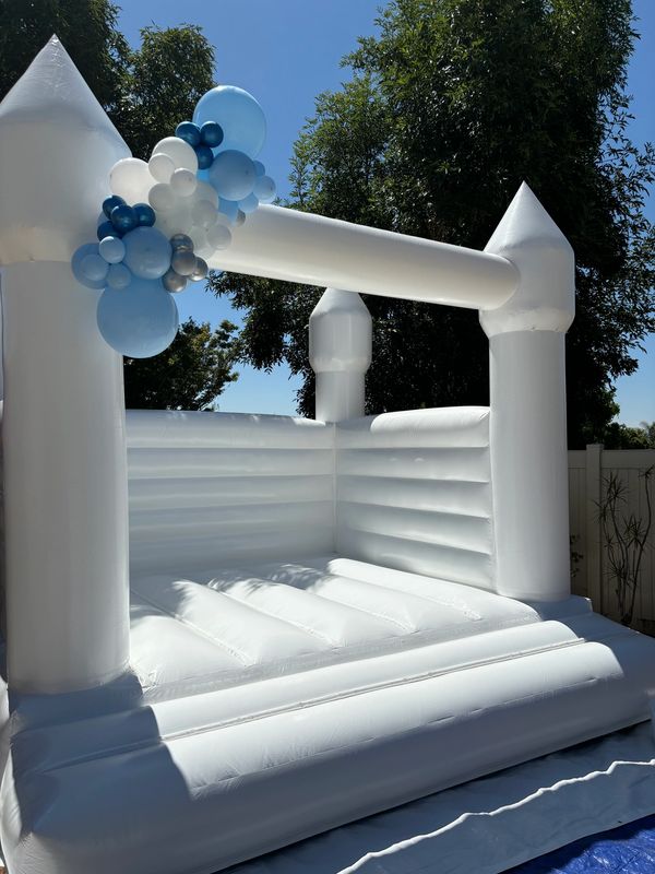 All white modern bounce house with a balloon garland draped across the upper corner