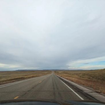 Open road stretching through flat plains under a cloudy sky.