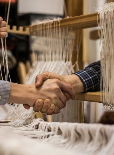 Two people's hands grasping each other through a weaving loom