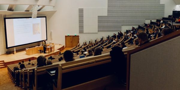 Hörsaal während einer laufenden Vorlesung, ein Dozent hält eine Präsentation vor vielen Studenten