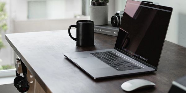 Aufgeklappter Laptop auf einem Schreibtisch mit einer schwarzen Tasse und einer weissen Maus daneben