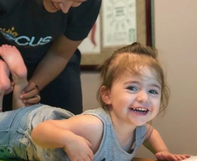 Smiling toddler lying on a play mat with an adult.