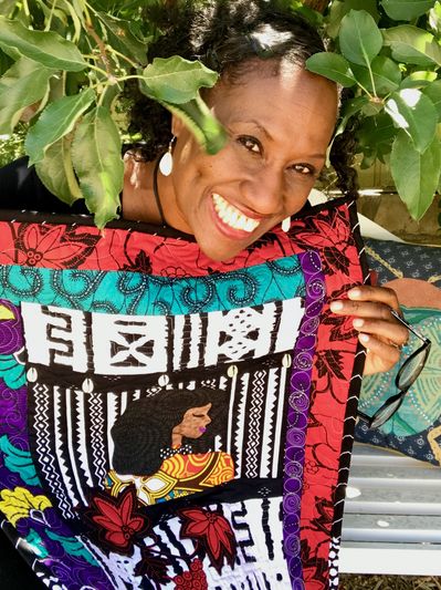 A smiling woman holds a vibrant, colorful fabric with artistic patterns and a portrait.