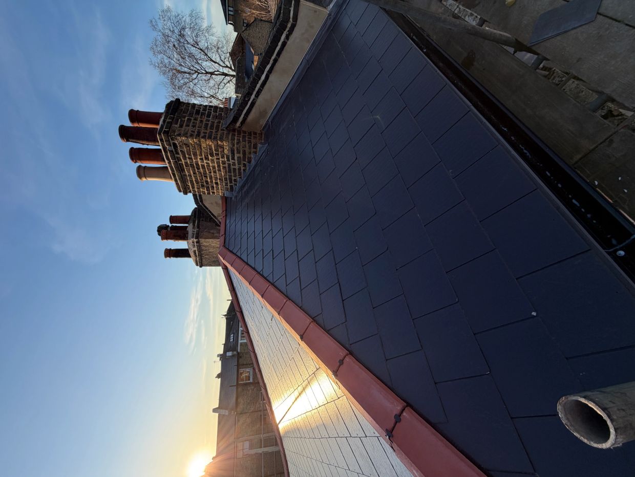 Sunset over a rooftop with brick chimneys and slate tiles.