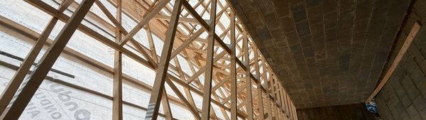 Wooden roof trusses under construction with translucent sheeting above.