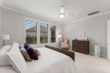 Spacious primary bedroom with neutral tones, crown molding, and plantation shutters that allow for a