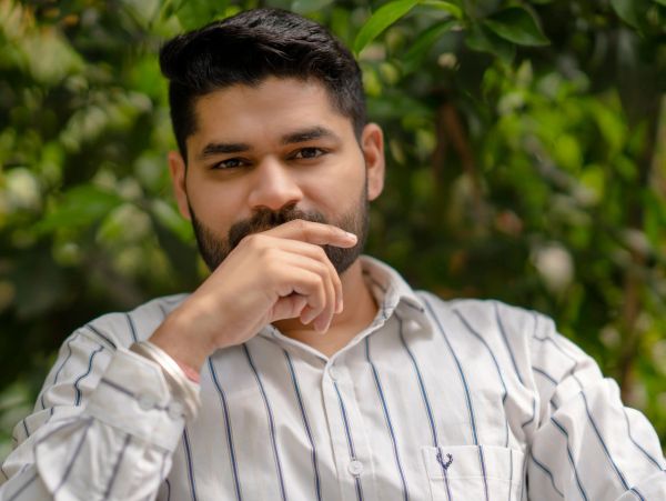 Man with beard in a striped shirt posing thoughtfully outdoors.