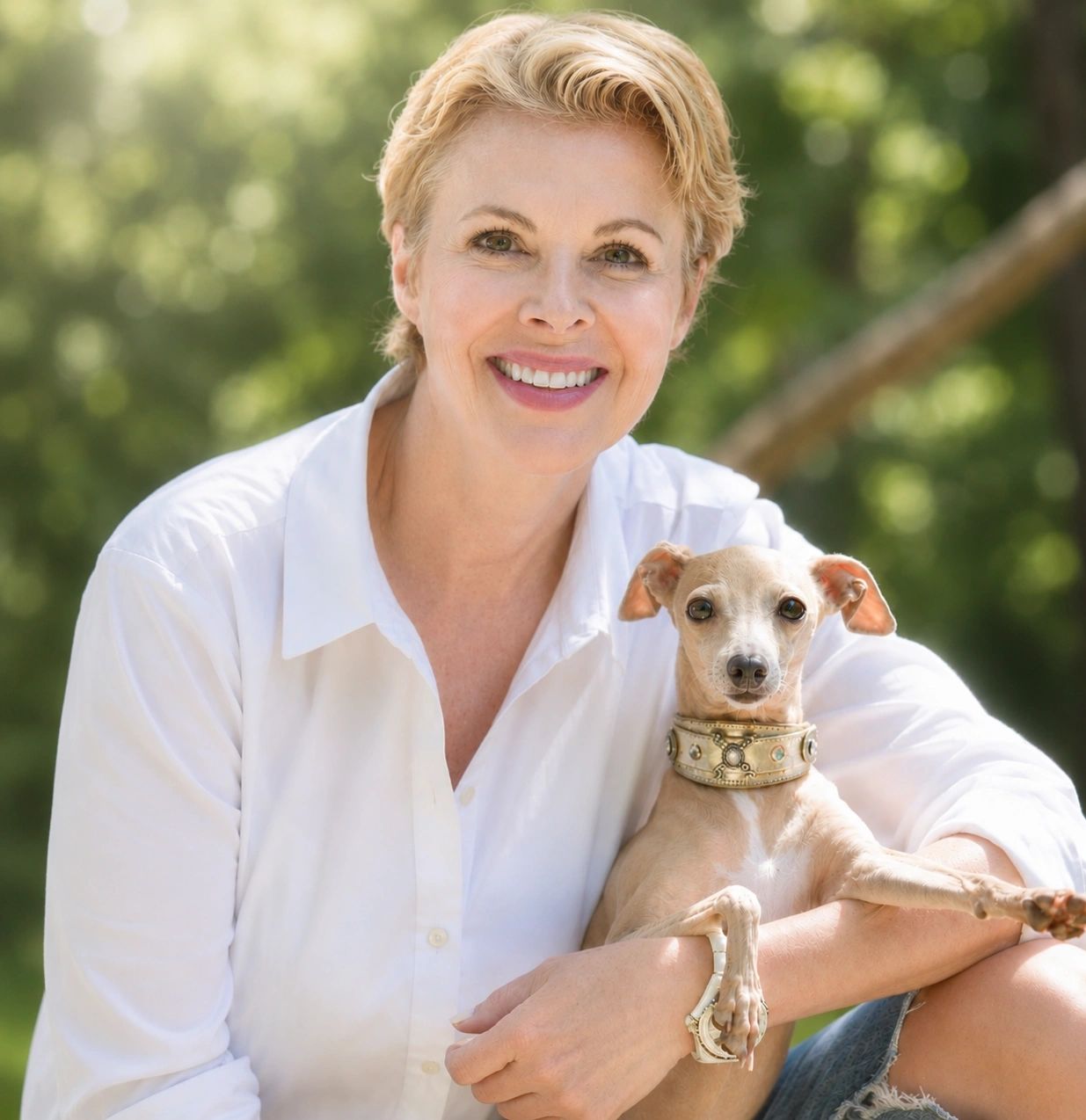 Smiling woman in white shirt holding a small dog with a decorative collar.