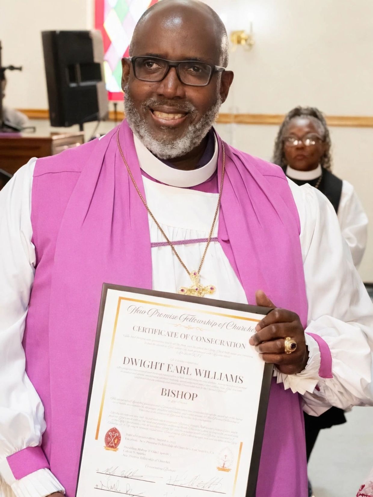 Man in religious attire holding a consecration certificate and smiling.