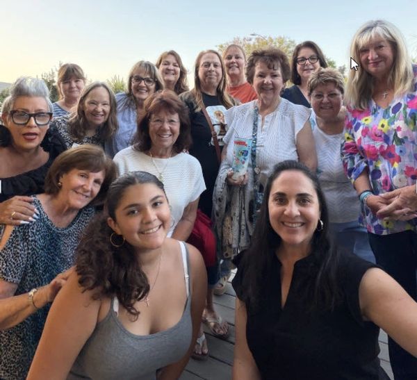 A joyful group of women posing together outdoors in casual attire.
