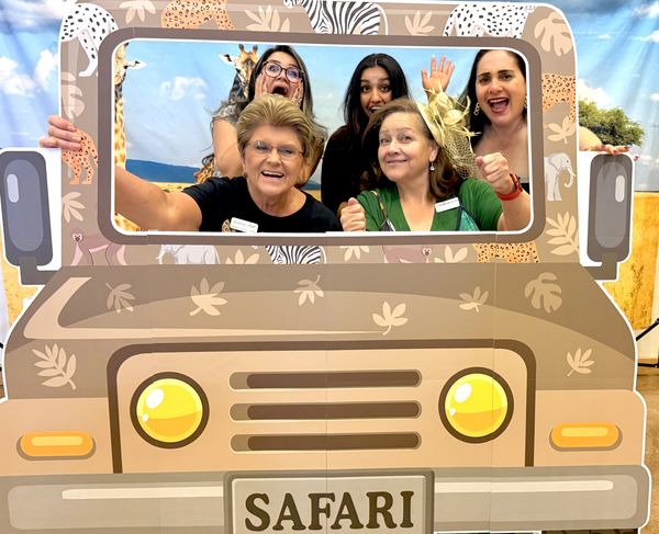 Five women posing happily inside a safari-themed photo frame.