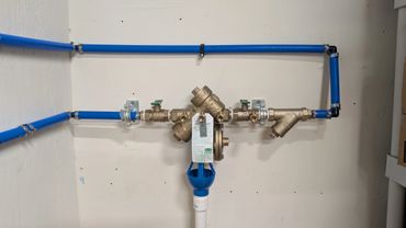 Blue pipes connected to a brass valve assembly mounted on a white wall.