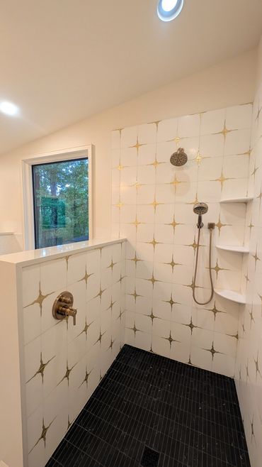 Modern shower with gold-accented white tiles and black floor tiles.